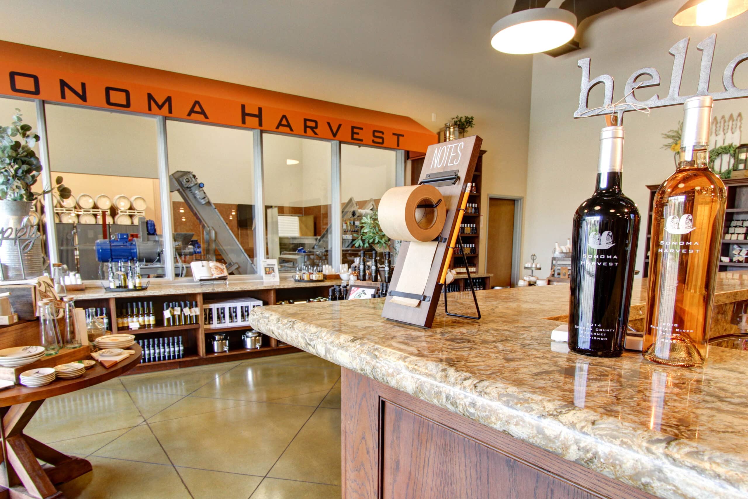 Sonoma Harvest Tasting Room image focused on wine bar. Features two Sonoma Harvest wine bottles and the background showcases merchandise.
